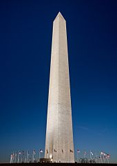 A dusk picture of the Washington Monument obelisk with flags around the base, in Washington, D.C.